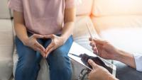 A photo of a physician sitting across from a patient, who is sitting on a sofa